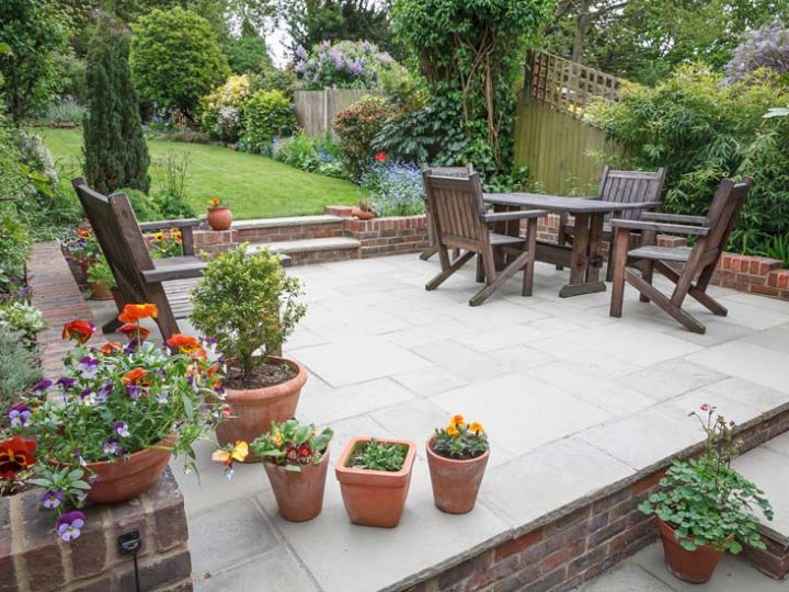 garden patio slab with a set of wooden chairs and table, and potted flowering plants